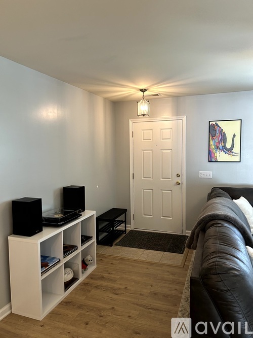 A living room with a black leather couch, a white entertainment center with a television and a black speaker, a white door, and a framed picture on the wall.