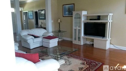 A living room with a white couch, a glass coffee table, and a television on a stand.