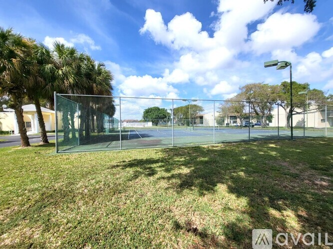 A tennis court is surrounded by a fence and palm trees.