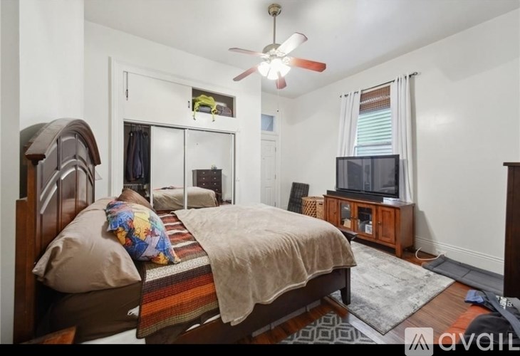A bedroom with a bed, a television, and a ceiling fan.