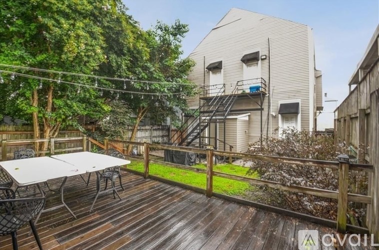 A wooden deck with a table and chairs is surrounded by a fence and trees.