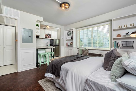 A bedroom with a large bed and a kitchen area in the background.