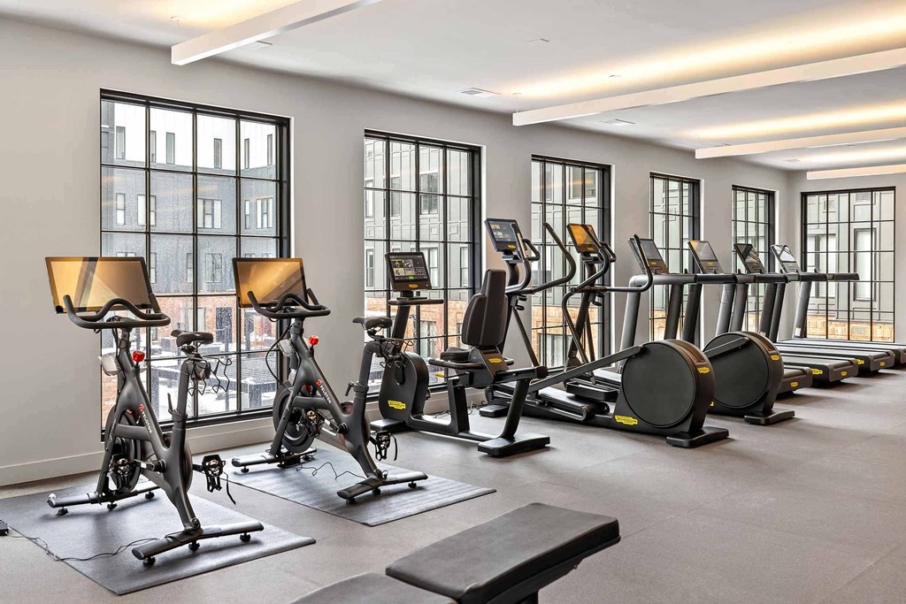 A gym with a row of exercise bikes and elliptical machines.