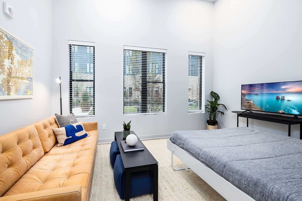 A living room with a yellow couch, a grey bed, and a painting on the wall.