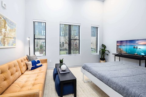 A living room with a yellow couch, a grey bed, and a painting on the wall.