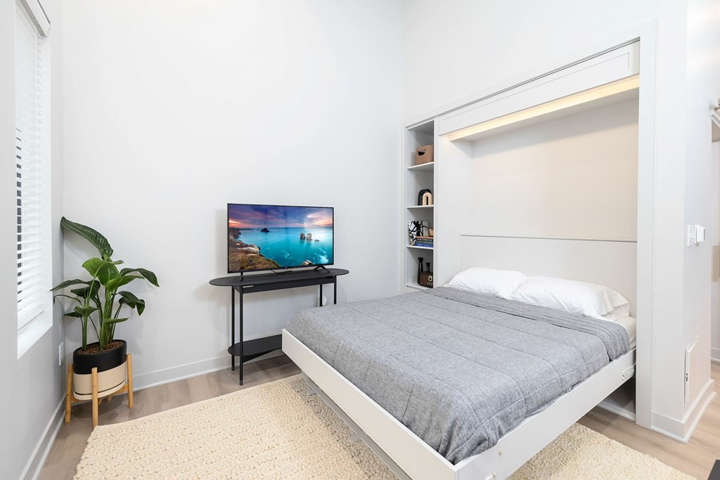 A bedroom with a bed, a small table with a television on it, and a potted plant.