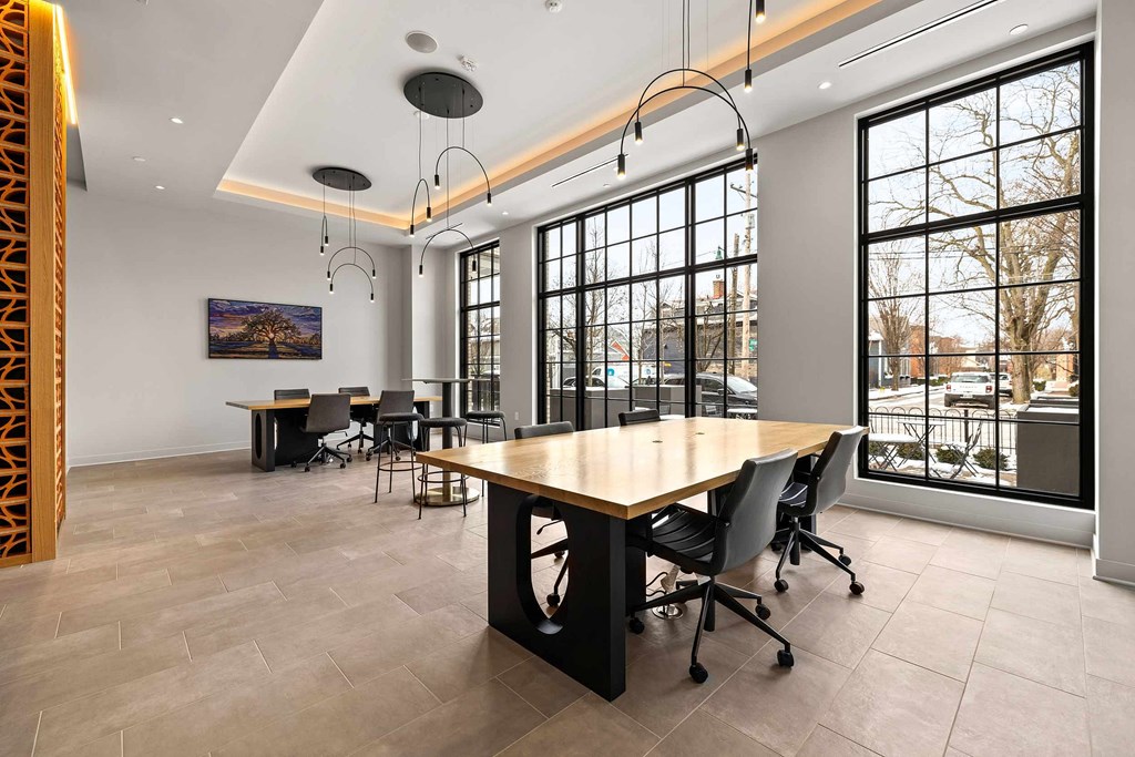 A conference room with a long table and chairs, a painting on the wall, and a view of the outside through large windows.