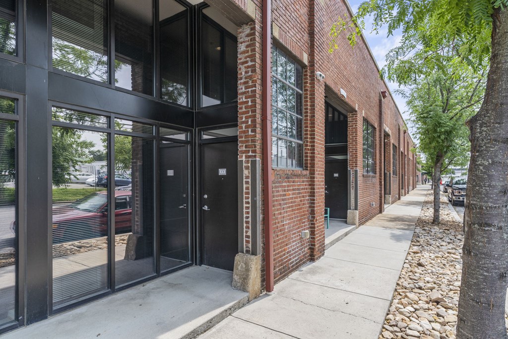 the side of a brick building with glass windows and a sidewalk