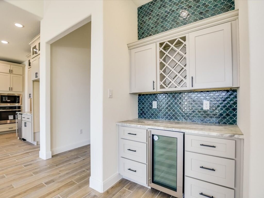 A kitchen with white cabinets and a green backsplash.