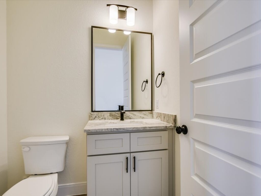 A white toilet sits next to a marble countertop with a mirror above it.