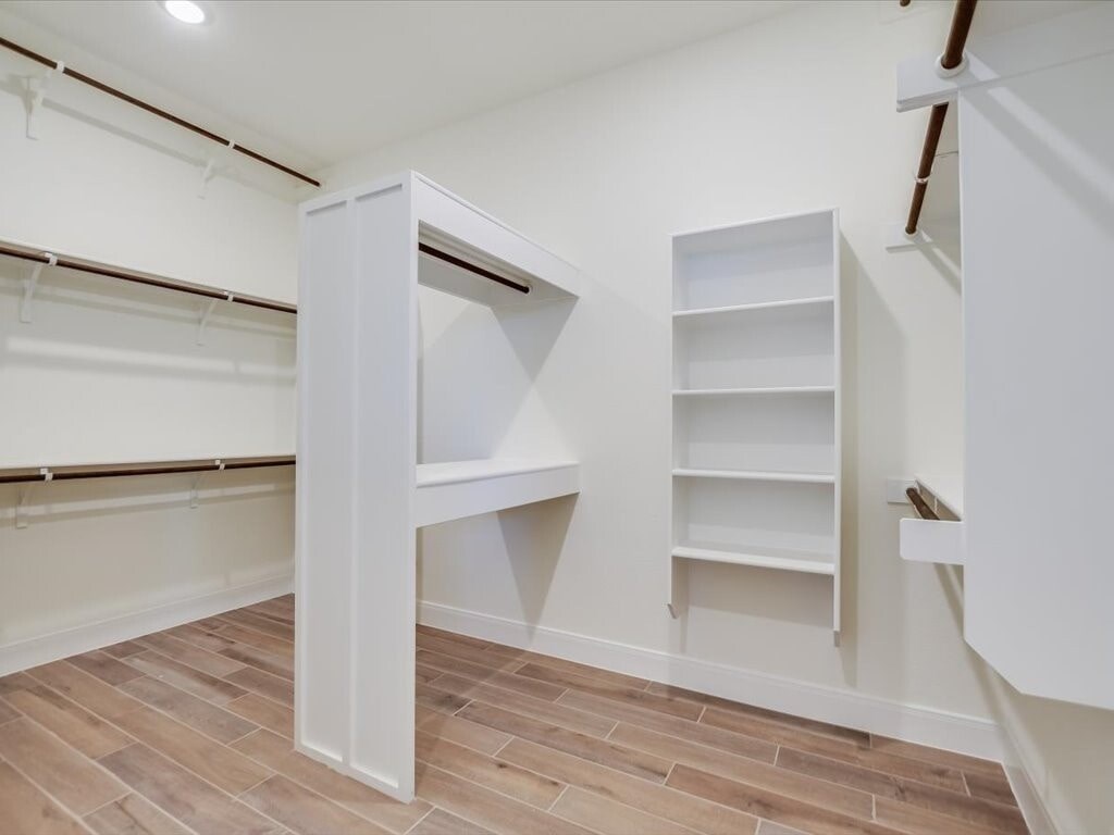 A white closet with shelves and a wooden floor.