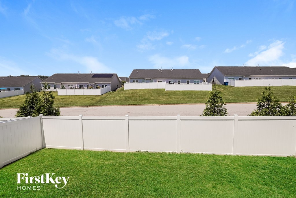 A white fence separates a grassy area from a row of houses.