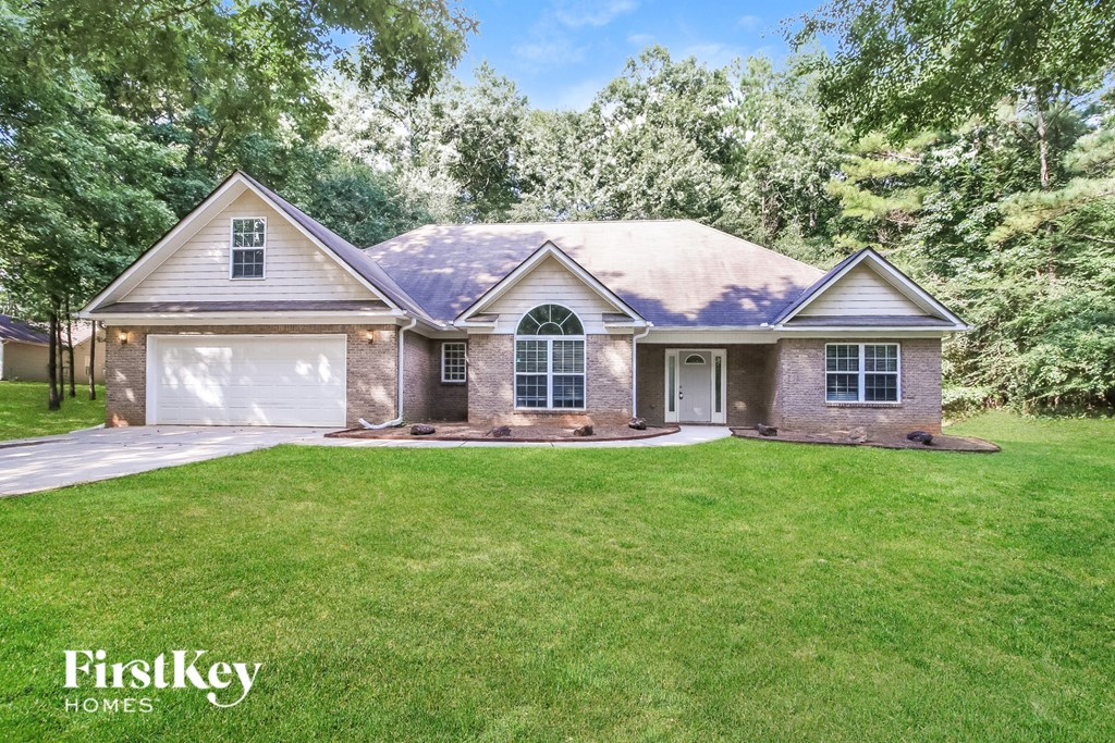 A house with a brown roof and a white garage door is surrounded by greenery.