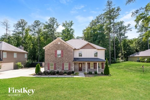 A brick house with a porch is surrounded by green grass and trees.