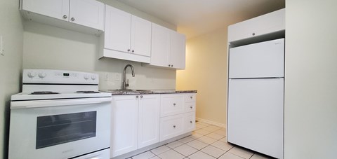 A white kitchen with a stove, sink, and refrigerator.