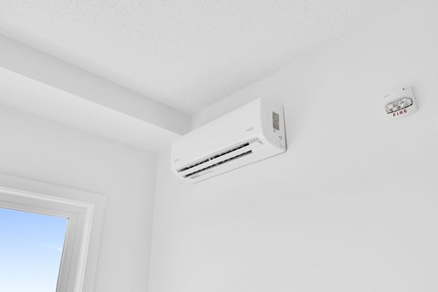 A white air conditioner is mounted on a white wall next to a window.