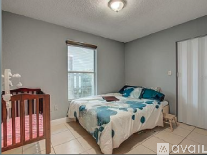 A bedroom with a bed, a crib, and a window.