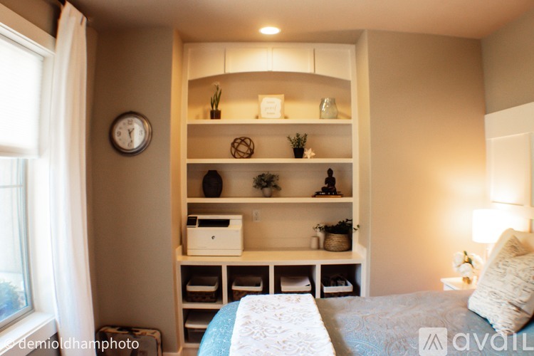 A bedroom with a bed, a window, a clock, and a shelf with various items.