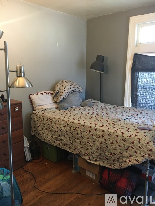 A bed with a floral comforter sits in a room with a lamp and a window.
