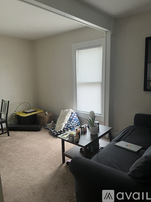 A living room with a black couch, a small table, and a window with blinds.