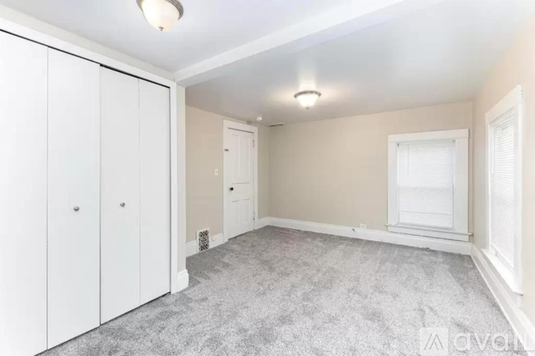 A bedroom with a grey carpet and white cupboards.