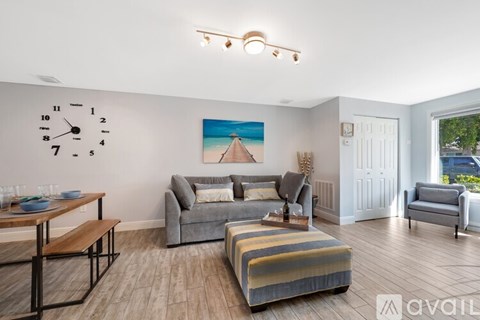 A living room with a grey couch, a wooden table, and a painting of a beach scene on the wall.