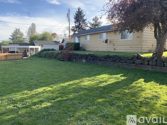 A grassy backyard with a stone wall and a house in the background.