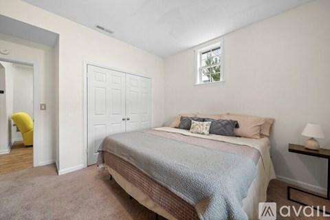 A bedroom with a bed, a yellow chair, and a nightstand with a lamp.