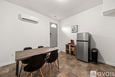 A kitchen area with a table and chairs, a refrigerator, and a trash bin.