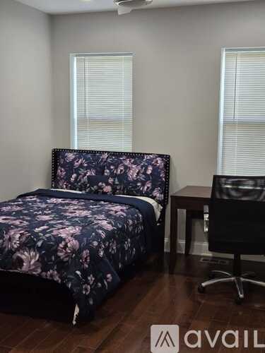 A bedroom with a floral bedspread and a black office chair.