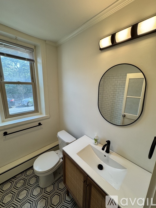 A bathroom with a toilet, sink, mirror and window.