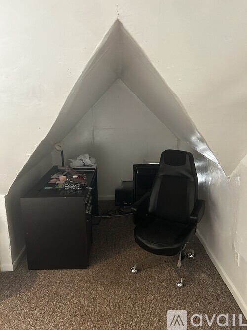 A black chair is in a corner of a room with a white wall.