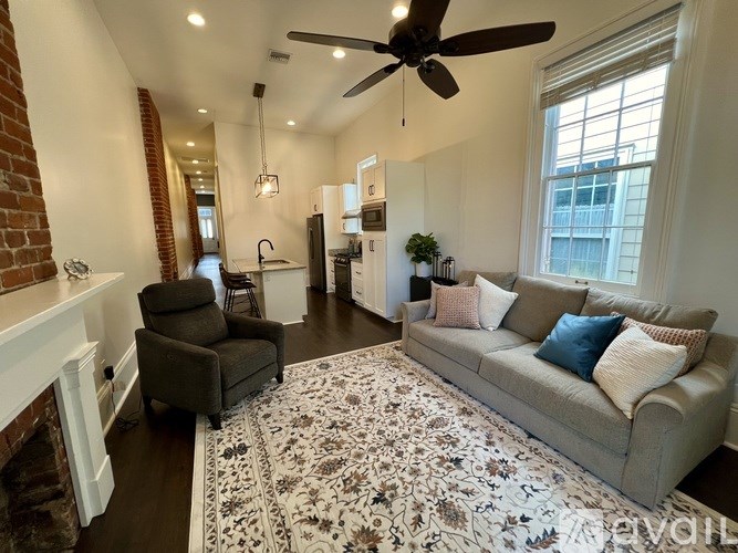 A living room with a grey couch, a fan, and a rug.