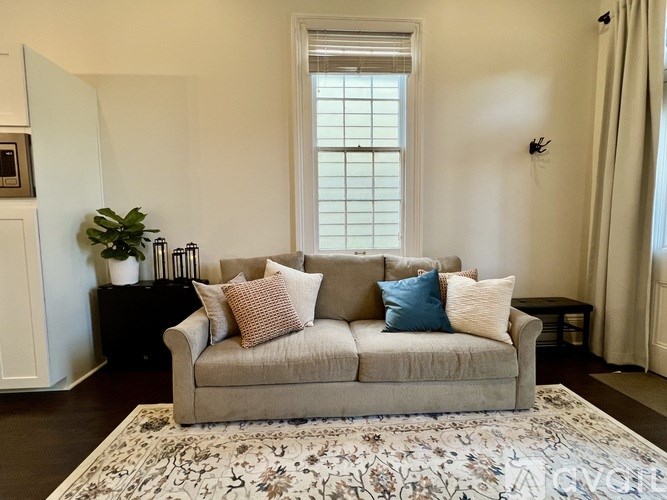 A beige couch with pillows sits in front of a window in a room.