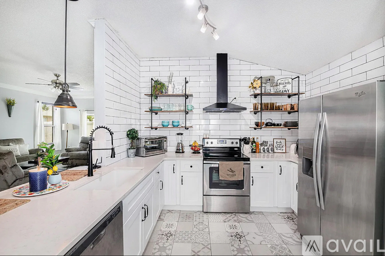 A modern kitchen with a stainless steel refrigerator, a black range hood, and a white tiled backsplash.