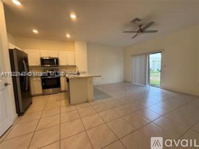 A spacious kitchen with a refrigerator, microwave, oven, and a ceiling fan.