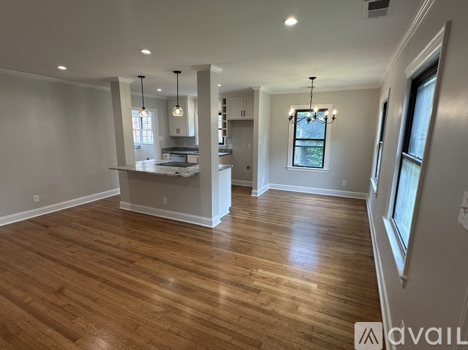 A spacious room with wooden flooring and a kitchen area in the background.