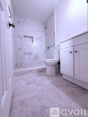 A white bathroom with marble tiles and a toilet.