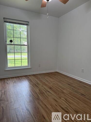 A room with wooden flooring and a window overlooking a green area.