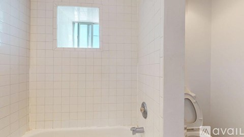 A white tiled bathroom with a window in the shower.