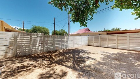 A backyard with a fence, a tree, and a house in the background.