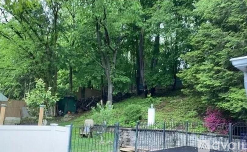 A green hill with trees and a white fence.