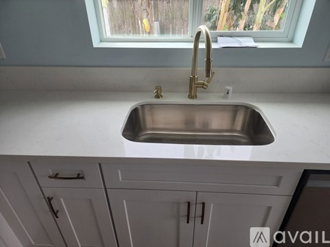 A kitchen sink with a gold faucet and a window above it.