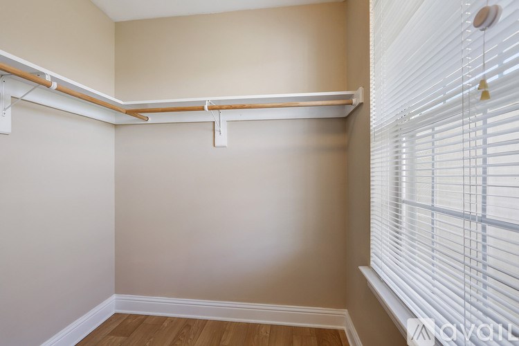 A room with a white ceiling, wooden floor, and white walls with a window covered in blinds.