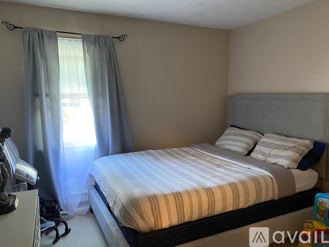 A bedroom with a bed, pillows, and a window with curtains.