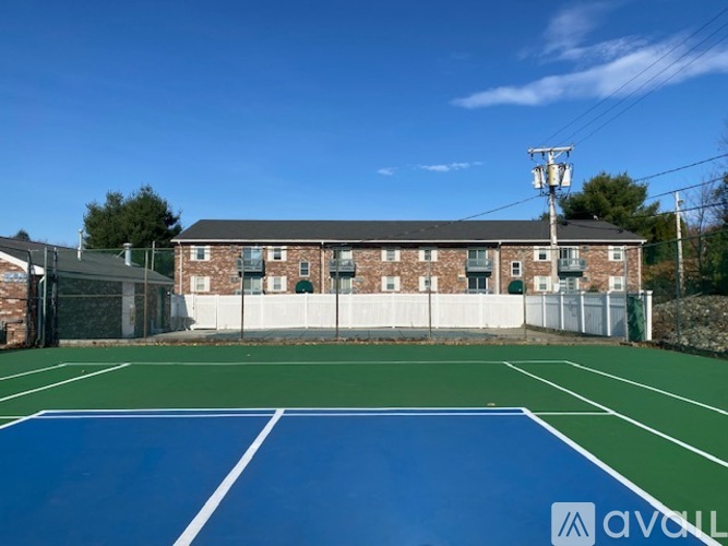 A tennis court with a blue surface and white lines, surrounded by a brick building and a fence.