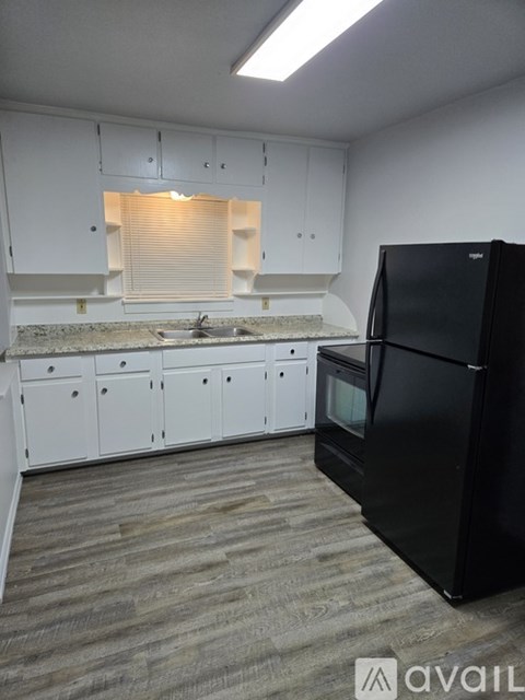A black refrigerator stands in a kitchen with white cabinets and a marble countertop.