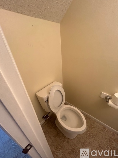A toilet in a small bathroom with a white wall.