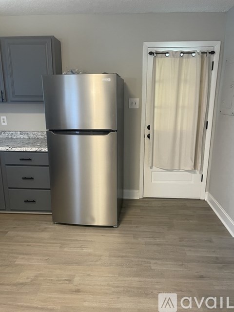 A stainless steel refrigerator in a kitchen with a white door and a white curtain.