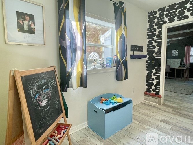 A chalkboard with a drawing of a face is leaning against a wall next to a window with curtains.